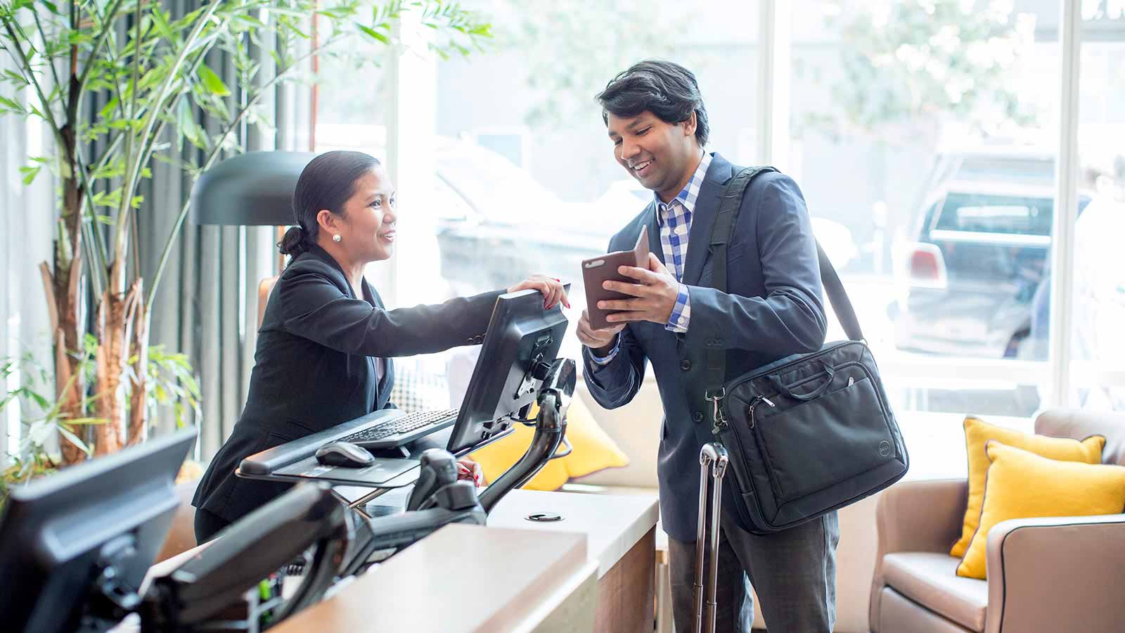 A man showing his mobile phone to a woman at the concierge desk.